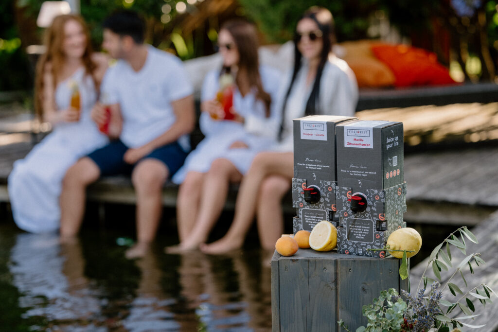 Junge Erwachsene sitzen am Steg und genießen FREIGEIST-Getränke am Wasser