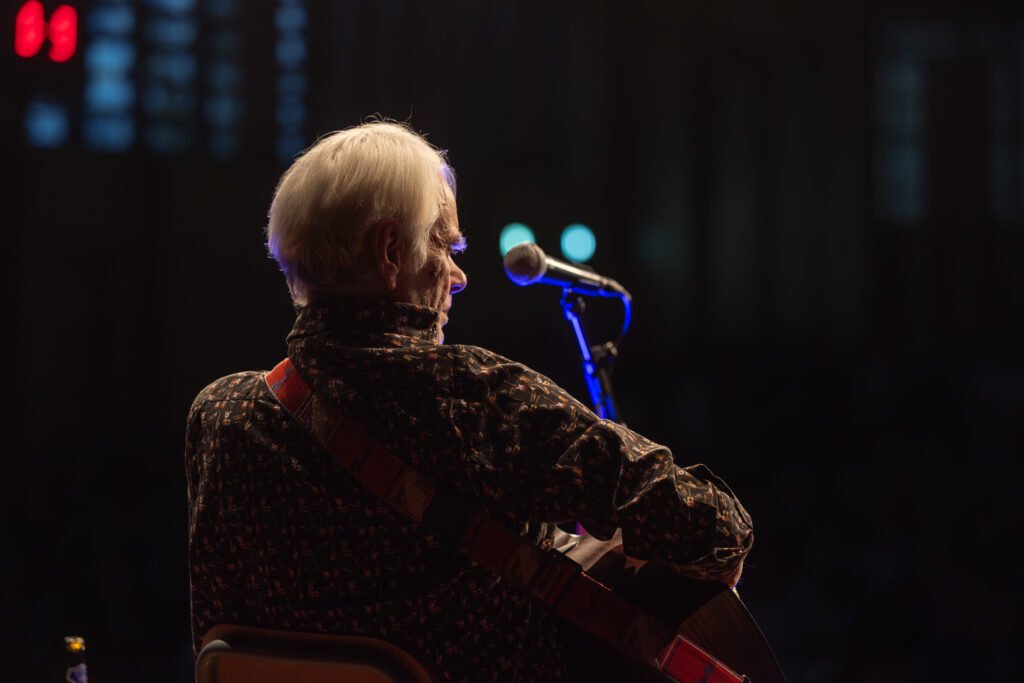 Älterer Musiker mit Gitarre am Mikrofon auf der Bühne