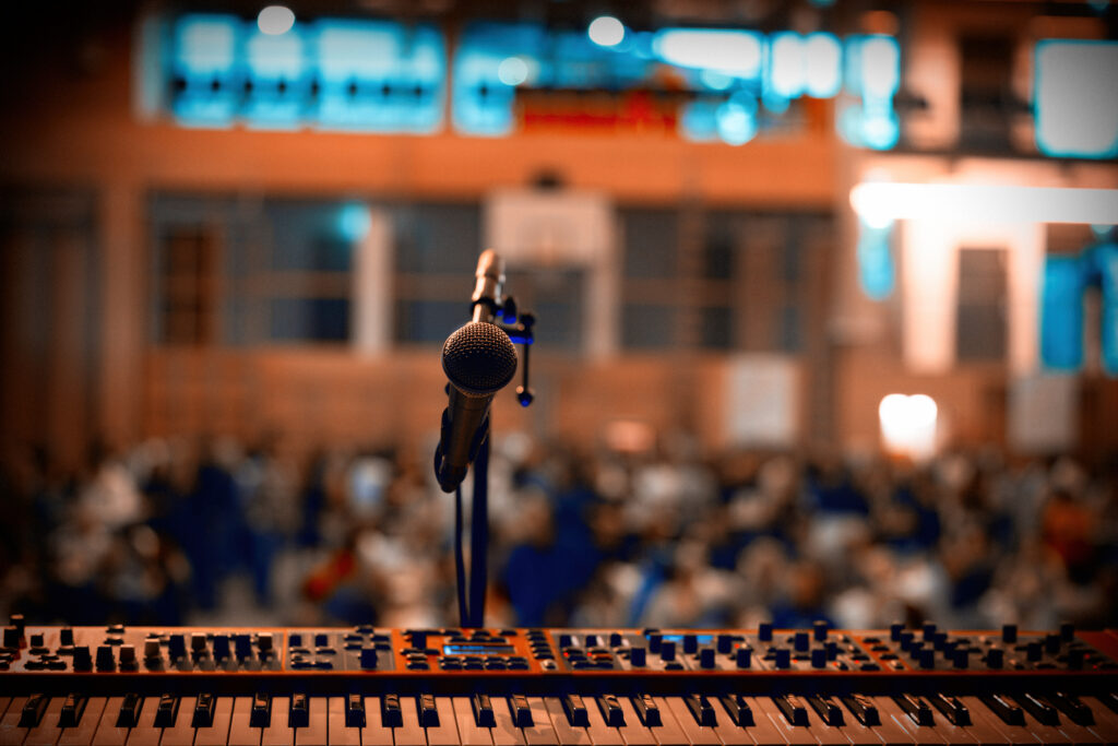 Mikrofon vor Keyboard mit unscharfem Publikum im Hintergrund