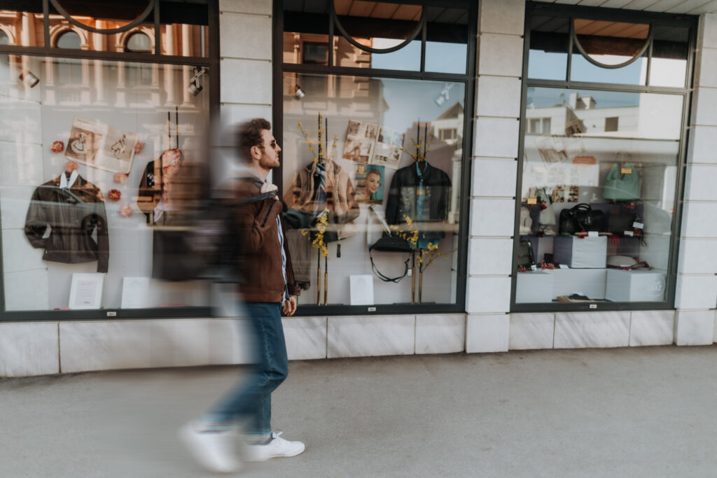 Ein Mann spaziert an einem Schaufenster von Stoichart Leder vorbei, das mit Lederjacken, Accessoires und Frühlingsdeko gestaltet ist.