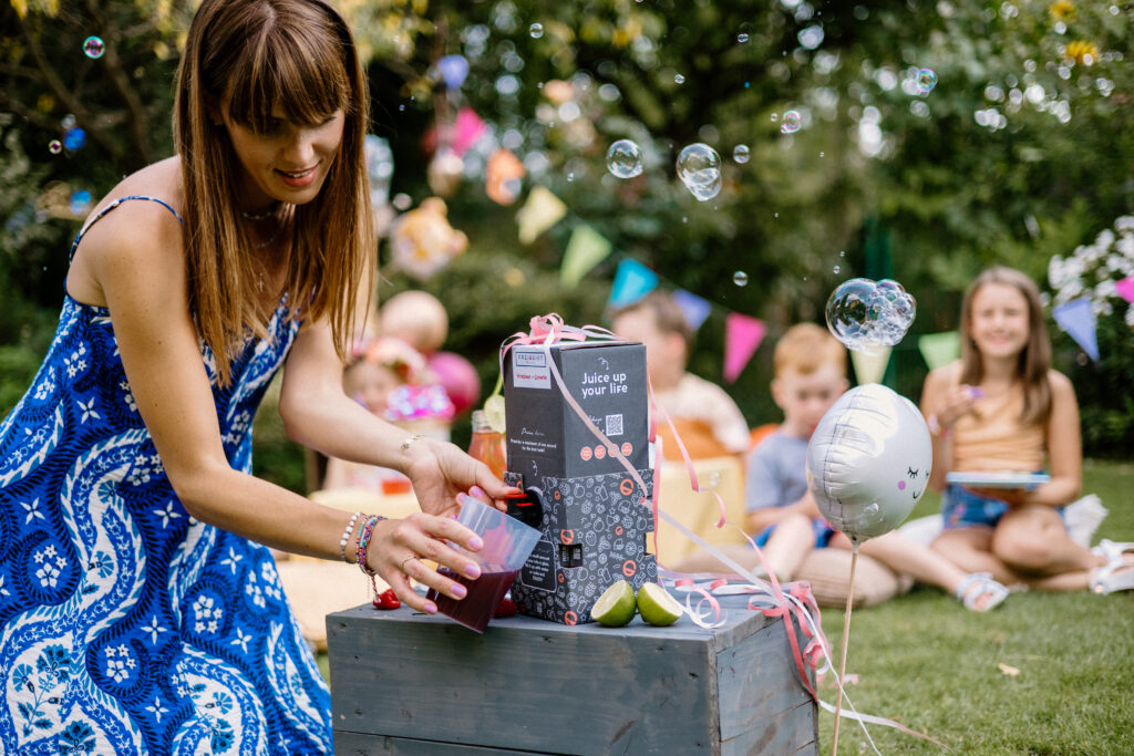 Frau schenkt FREIGEIST Himbeer-Limette in einen Becher bei einer Gartenfeier mit Kindern