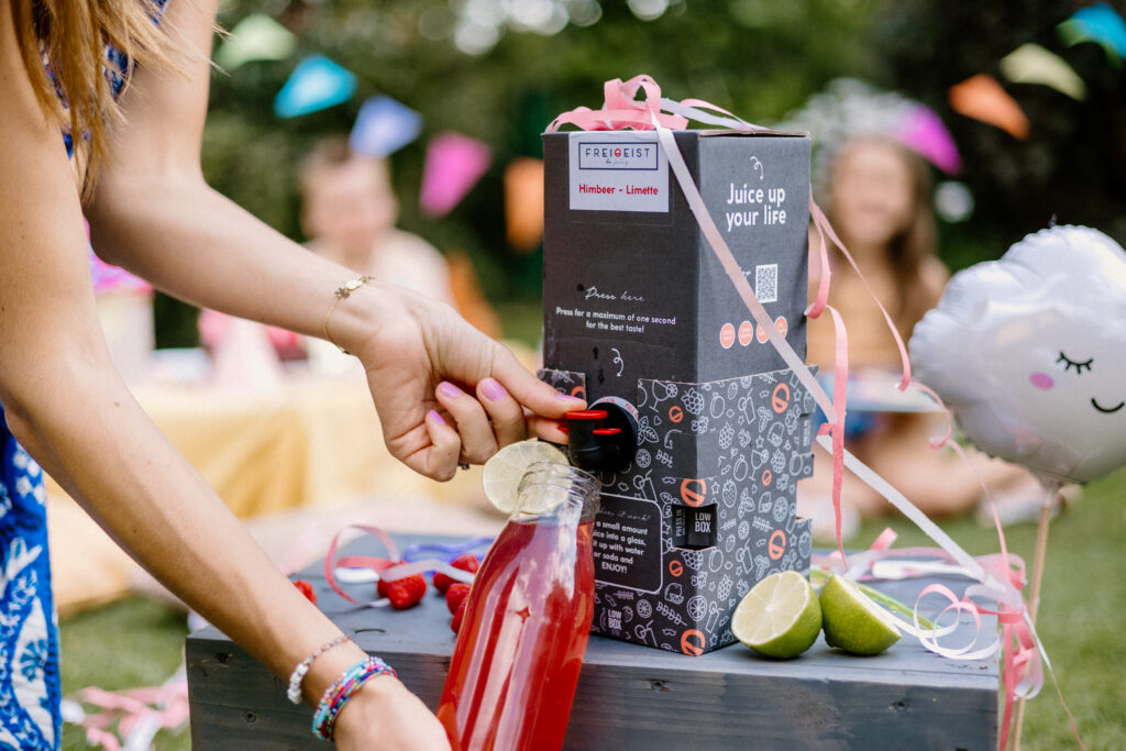 Nahaufnahme vom Einschenken von FREIGEIST Himbeer-Limette in eine Glasflasche mit Limetten und Deko