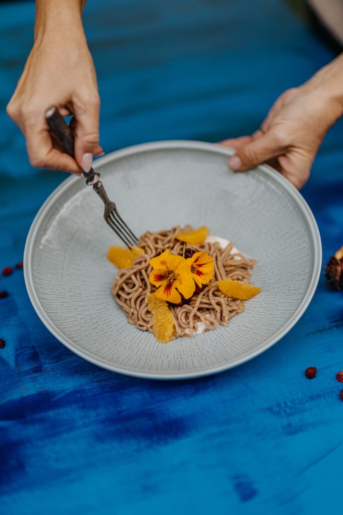 Herbstliches Dessert aus Maronipüree mit Orangenfilets und essbaren Blüten – kunstvoll angerichtet im Deli Leibnitz.