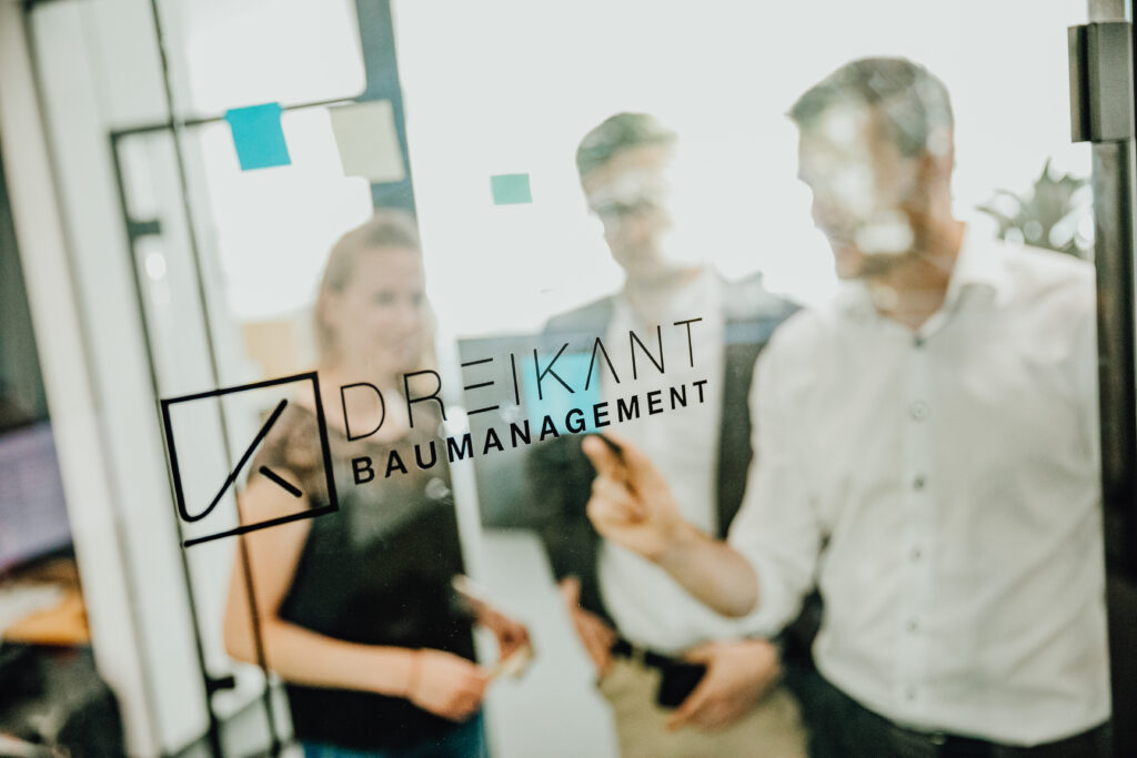 Team von DREIKANT Baumanagement steht hinter einer Glastür mit Logo-Aufschrift