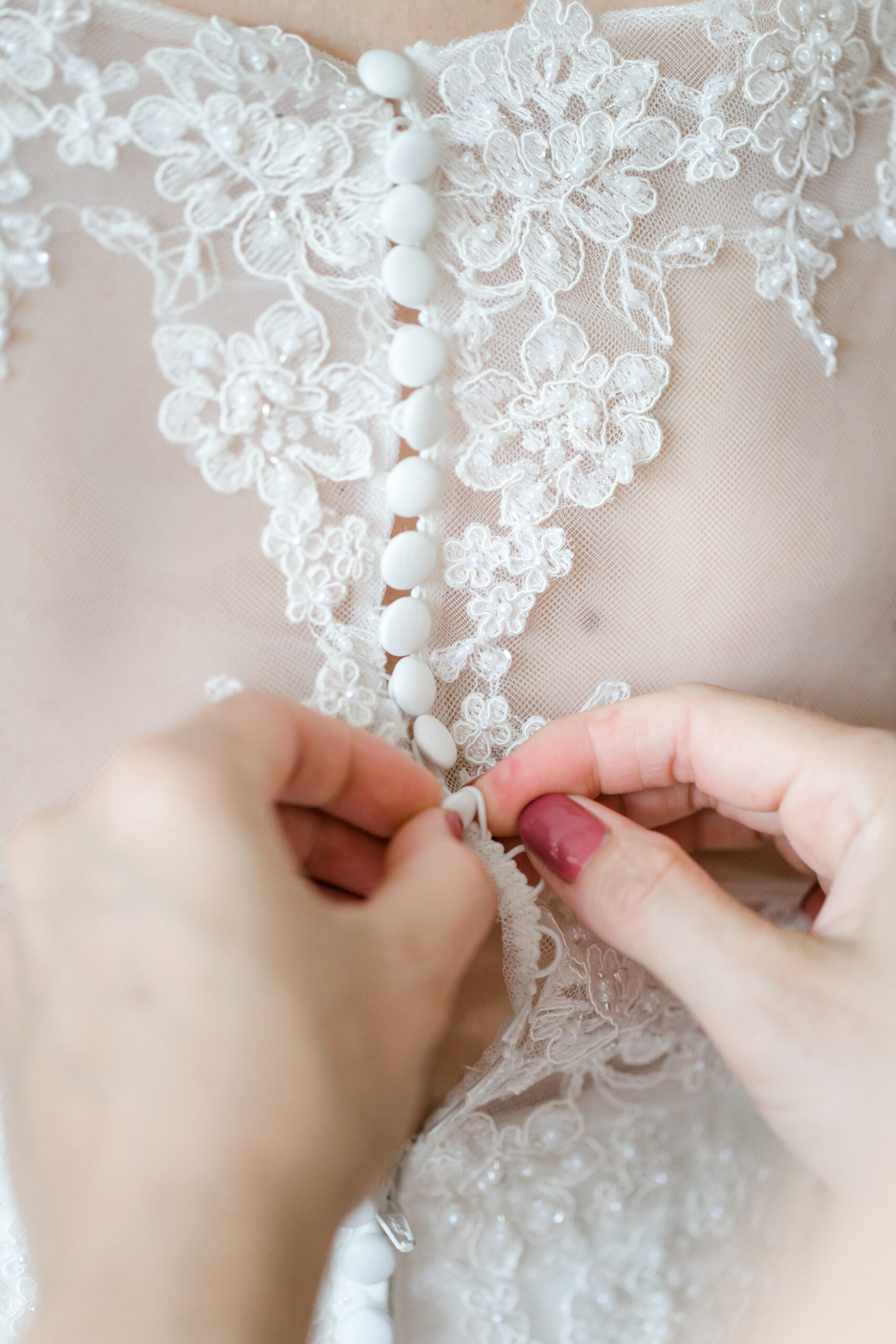 Detailaufnahme: Hände schließen Spitzenknöpfe am Brautkleid.