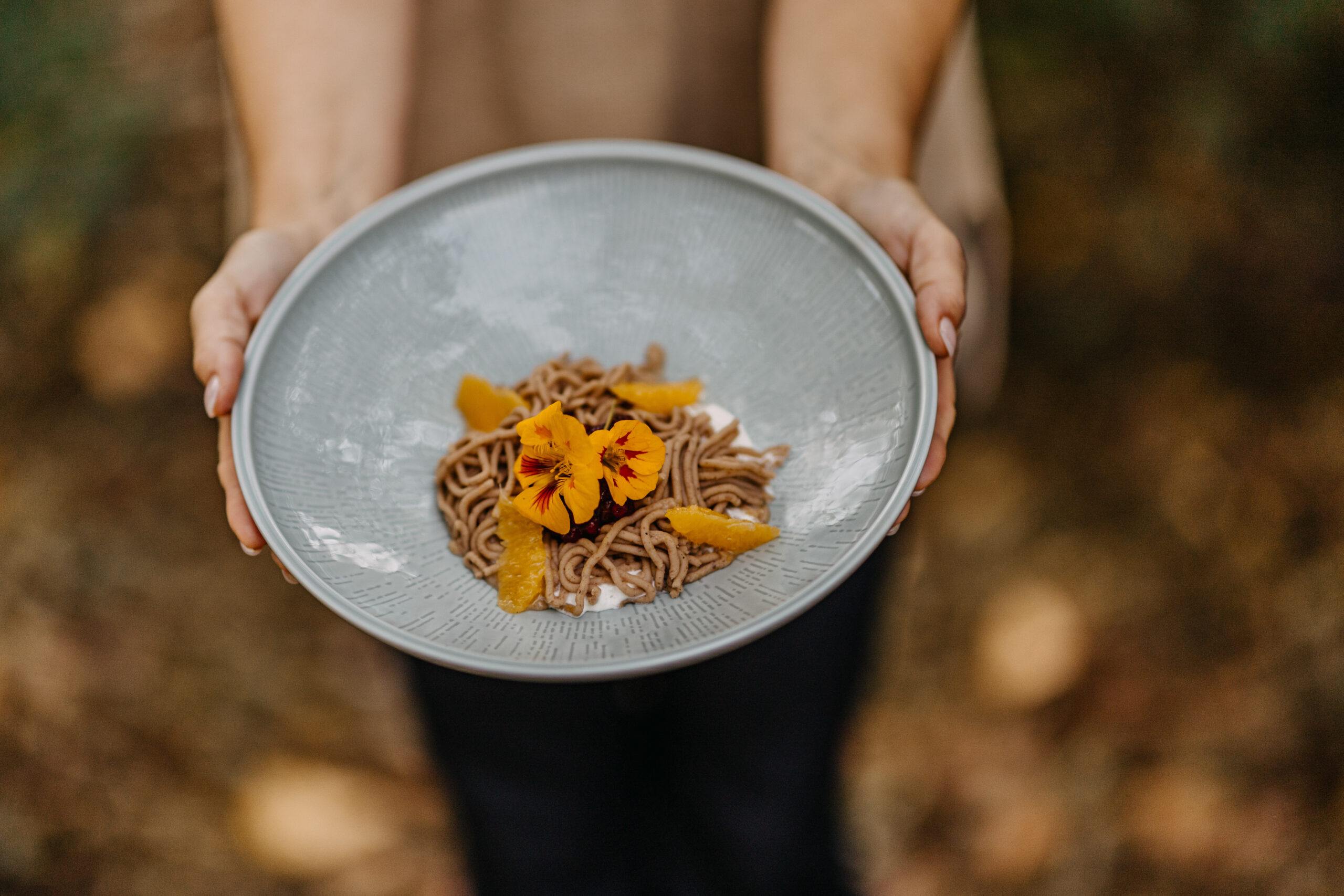 Herbstliches Dessert aus Maronipüree mit Orangenfilets und essbaren Blüten – kunstvoll angerichtet im Deli Leibnitz.